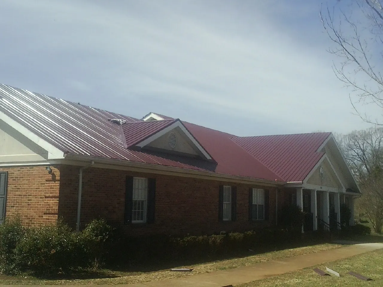 Red metal roof with gabled entries on a long brick building, from a Hail Damage Roof Repair job in Fort Payne