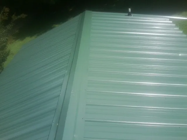 New green metal panels meeting at the ridge of a roof — Flat Roof Repair work by our crew in Fort Payne