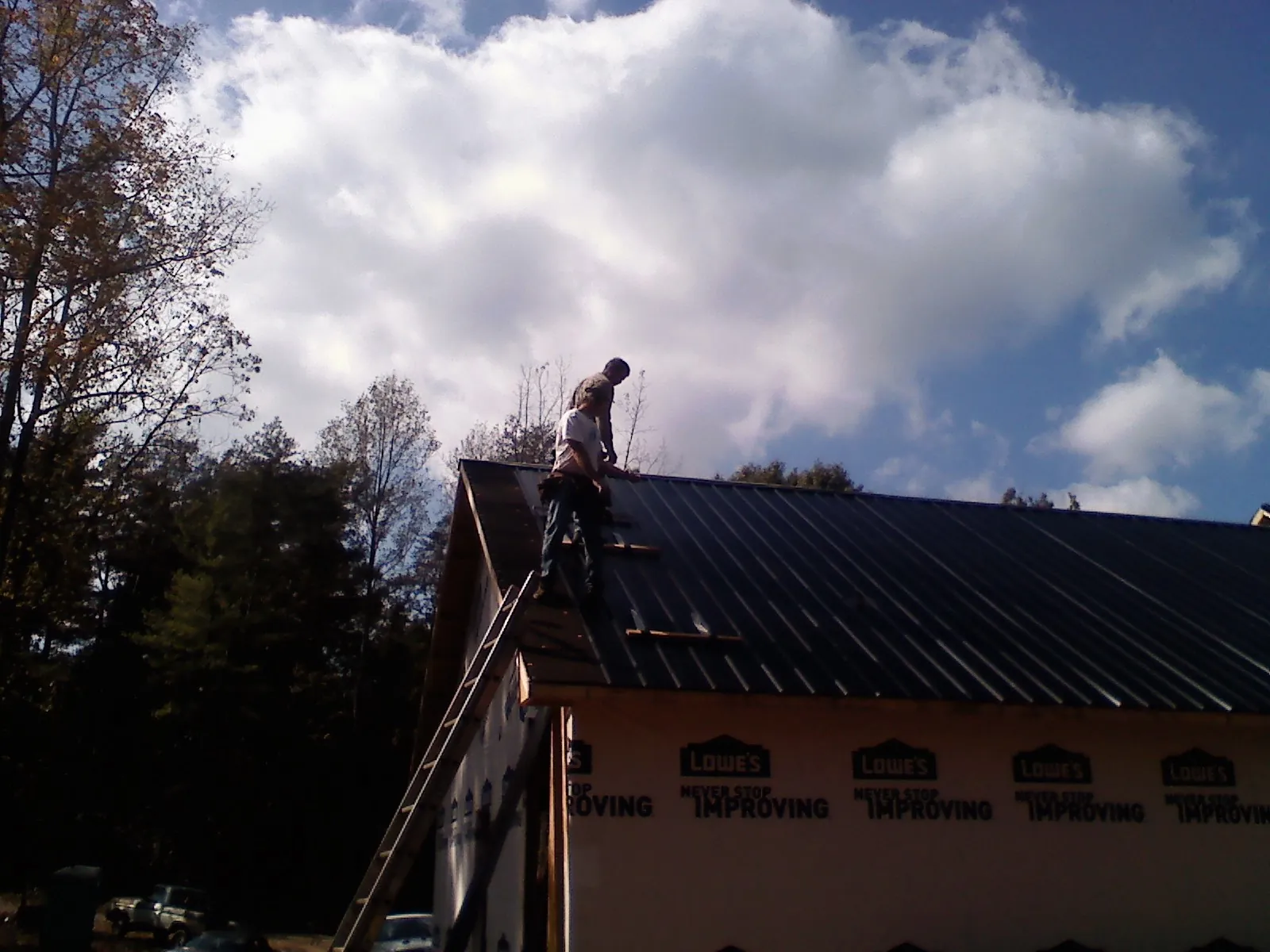 Roofer fastening dark metal panels high against a cloudy sky, from a Roof Inspection job in Fort Payne