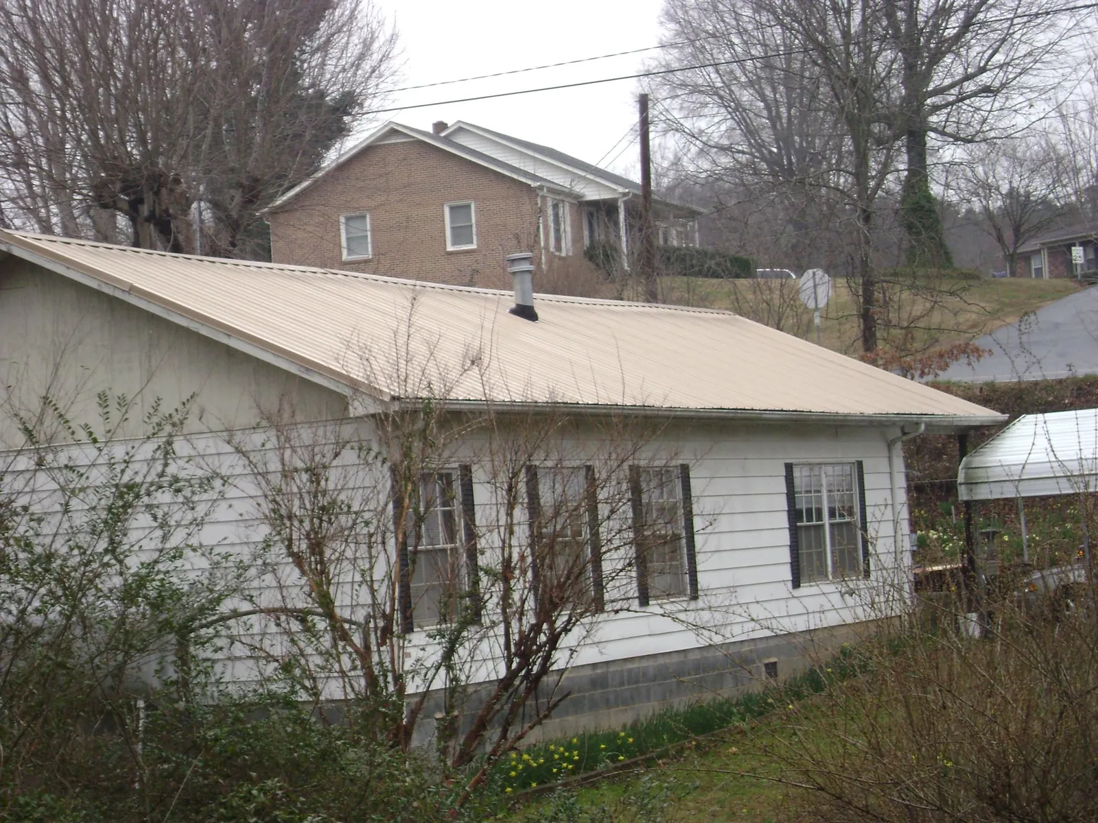 Tan metal roof on a white sided house set into a hillside — Commercial Roofing by Roofing Brothers in Fort Payne