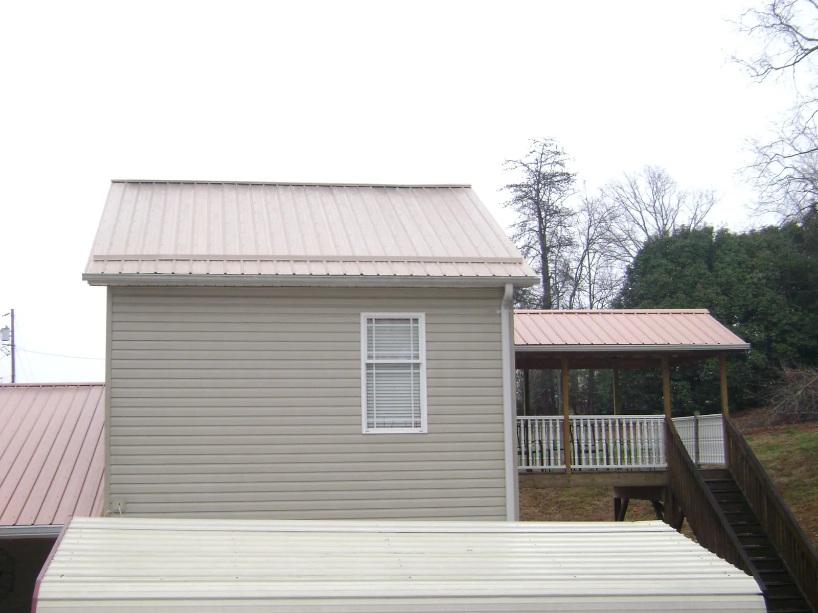 Tan metal roofs on a two story addition and attached porch, from a Roof Replacement job in Fort Payne
